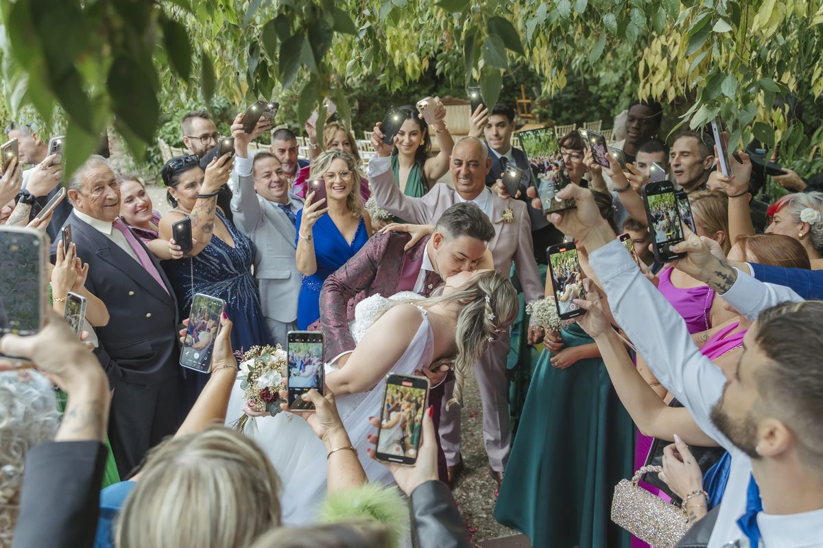 Novios besándose rodeados de invitados grabando con el móvil