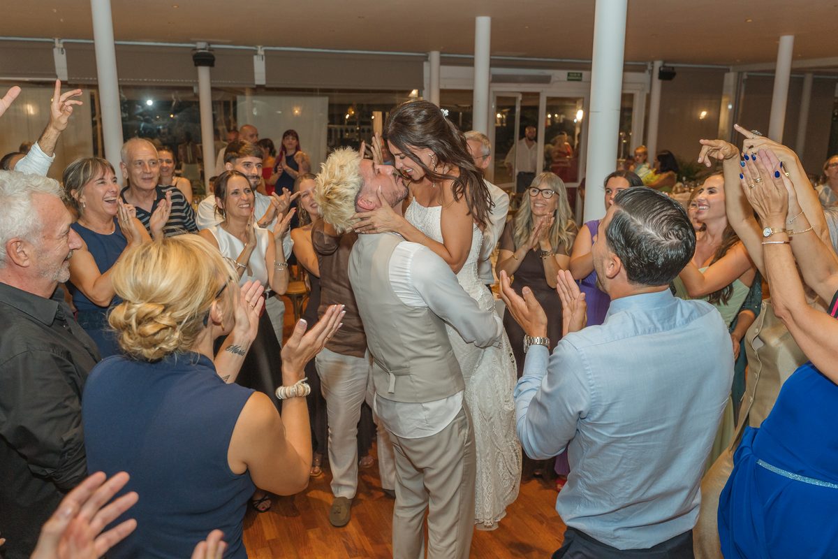 Novios besándose rodeados de invitados aplaudiendo en la pista de baile