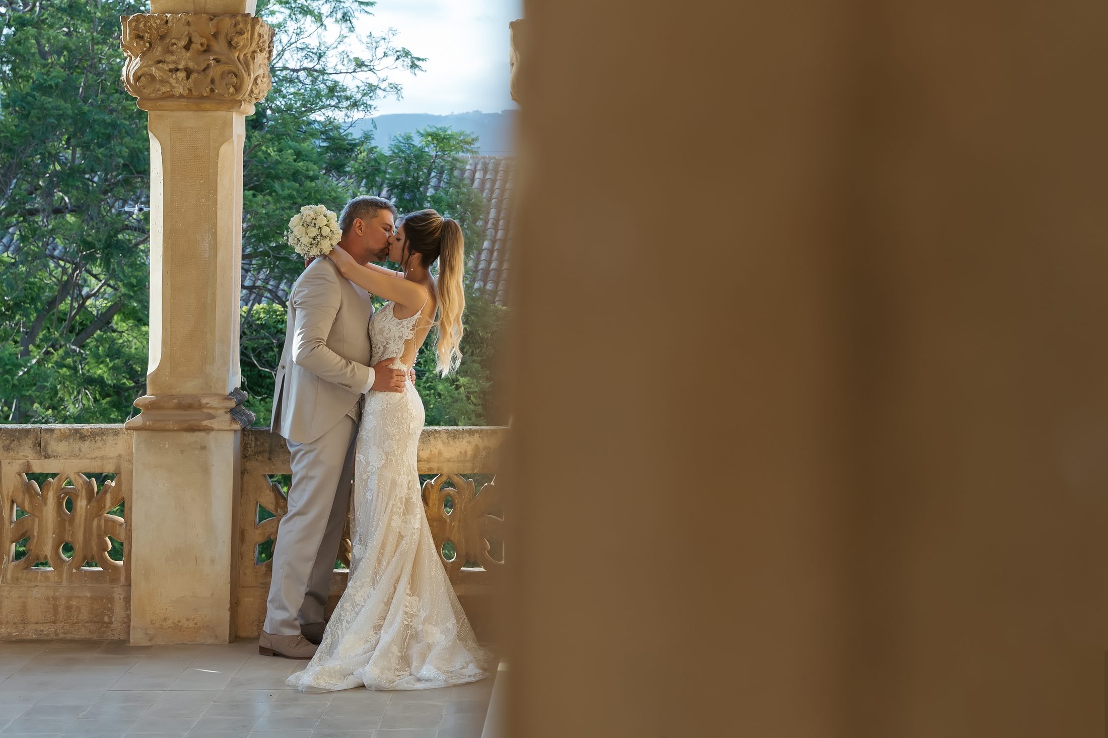 Novios besándose al atardecer en una terraza de piedra con columnas