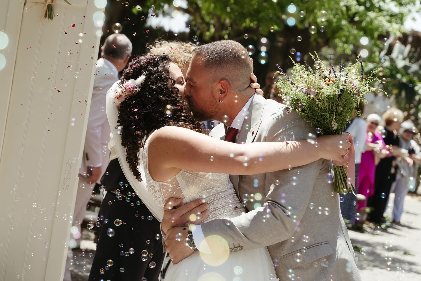 Novios besándose entre pompas de jabón y pétalos a la salida de la ceremonia